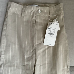 Randiga kostymbyxor  - Beige randiga kostymbyxor med hög midja och bootcut modell. Liten i midjan fast stretchigt material. Nyskick och aldrig använda. Prislapp kvar