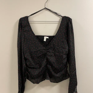 Låg V-ringad blus med öppen rygg och hjärt-mönster - Säljer den här för att jag tycker att den är väldigt opraktiskt. Den är väldigt fin men ärmarna åker ner hela tiden och snörena som finns vid ärm öppningarna kommer i vägen väldigt mycket. Jag önskar att jag kunde ha fått mer användning utav den :(