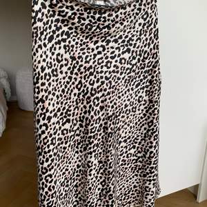 Silkig vadlång kjol i leopardmönster från Gina Tricot. Dämpad rosa/beige färg med svart mönster. Faller snyggt och smalnar av i midjan. Använd ett fåtal gånger i fint skick. 