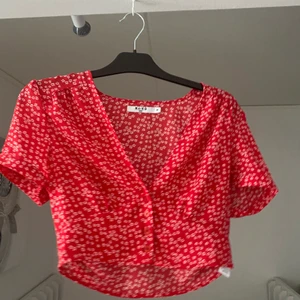 Röd blommig crop top - Röd croptop med vita blommor. Den knäpps framtill med 4 knappar. Kan bara fraktas :) 