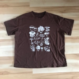 Brun t-shirt med svamptryck stolek L - En brun t-shirt med vitt tryck föreställande svampar. Tröjan är från shein och är i stolek L. Bra skick, köpte det för lite mindre än ett år sedan men har bara använt några gånger. Pris kan diskuteras. 