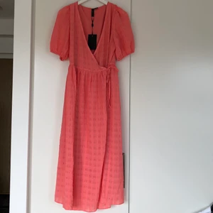 Omlottklänning - Persikofärgad strukturerad midiklänning. Omlott och puffärm. Aldrig använd, prislapp kvar. Normal i storlek. 