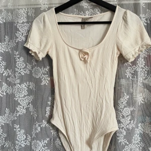 Body från H&M  - Söt creme färgad body från H&M. Köpte begagnat men i fint skick. Katt i hemmet. Köparen står för frakten. 