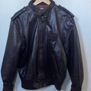 Läderjacka - Läderjacka från members only som jag köpte på secondhand i barcelona. Endast mindre skador, ser annars som ny ut. Mörkt brunt/rött/lila läder med vinrött innetyg Storleken är 38, men passar M i herrstorlekar och kan passa många beroende på önskad passform