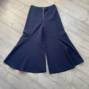 Topshop byxor - Marinblåa topshop byxor med rosé guldig kedja fram till. Vida ben som slutar strax innan ankeln. Hög i midjan och är i nyskick.