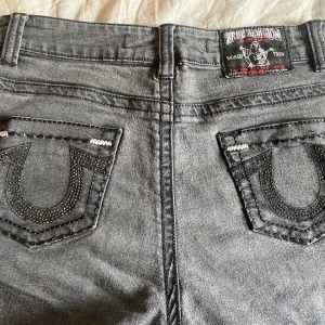 Svarta true religion jeans - Säljer mina svarta true religion jeans med glitter aktiga detaljer på fickorna. Byxorna är i storlek 33 men jag skulle säga att dom sitter bäst på någon med storlek XS då dom är korta för att vara storlek 33