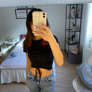 Svart tröja med fina blommor - Svart t-shirt med blommor och fin knytdetalj framtil. 