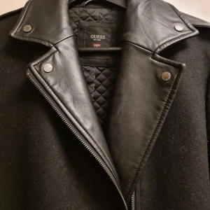 Guess kappa storlek S  - Svart kappa med läderdetaljer från Guess i storlek S.  Sparsamt använd.