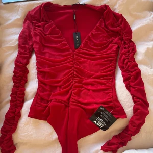 Röd body  - Helt ny body från Nelly. Röd med mesh ärmar. Storlek M   Kan mötas i Stockholm eller frakta , köparen står för frakt, inga returer