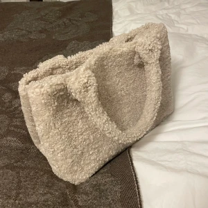 Teddy-väska från SAMSOE SAMSOE - Väska i teddy-tyg från SAMSOE SAMSOE. Längd 30cm, bredd 13cm, djup 20cm. Bra skick, anstånd fåtal gånger🤎Nypris 800kr