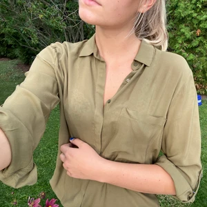 Grön skjorta - Grön skjorta från Pull & Bear. Ficka på ena sidan och ärmarna går att fästa med en knapp längre upp vid armvecket. Använd cirka 3 gånger. Fraktavgiften står köparen för!