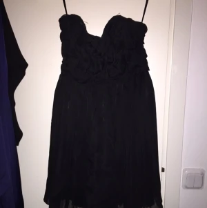  - Ärmlös klänning, svart. 
Med blommigtmotiv övertill - se bild 2.
Ganska kort 
Siden tyg med transparent tyg ovanför. 