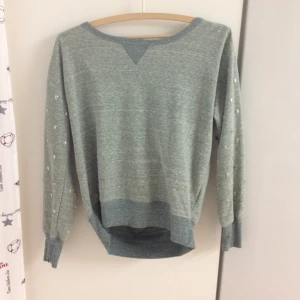 Härlig grön tröja med öppen rygg och dödskallar i silver som smyckar armarna.  - Härlig grön tröja med öppen rygg och dödskallar i silver som smyckar armarna. 