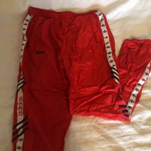  - röda adidas byxor i ”prassel” material, med vit rand och adidas logo längs båda benen. Stretchig resår så passar allt från storlek S till L
