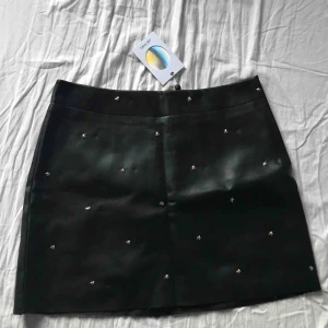 Skin kjol - Super snygg skinnimitations A-linje kjol från monki med matt läder och guldiga stjärnor. Har en dragkedja och knapp baktill samt en silkesaktig underkjol. Slutar vid 3/4 av låret. Högmidjad. Prislappen kvar så helt ny och aldrig använd.