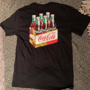 T-shirt med tryck  - Svart T-shirt med ett Coca cola tryck ifrån H&M (herr). ärmarna är lite längre än på en vanlig t-shirt. Storlek S