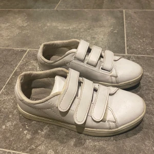 Vita sneakers - Vita sneakers med kardborreband från Nelly strl 37. Väldigt sköna och fint skick förutom små slitningar bak vid hälen som syns på bilder. På bilderna är de otvättade men tvättar såklart när någon köper!