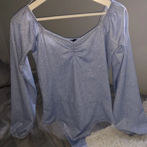 Långärmad body - Långärmad body i ljusblått med små vita fläckar. Bodyn har ”puff” armar, alltså lite större armar. Nästan helt oanvänd, säljer för att den inte används. Startbud börjar vid 120kr+frakt! Undrar ni något så är det bara att fråga på!