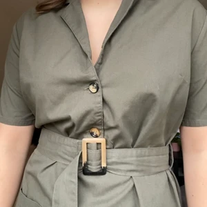 Militärgrön kort klänning - Klänning från NAKD i storlek 36 men snyggt bälte och i skjort-material. Funkar både till vintern med tunna strumpbyxor, och till sommaren! Endast använd 1 gång. 75kr exklusive frakt. 