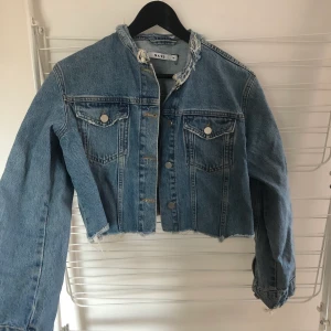 Croppad jeansjacka NA-KD 36 - Sliten croppad jeansjacka från NA-KD. Storlek 36. Jag har ej använt den. Köpte den här på Plick i somras. Skickar med postnords blåa kuvert
