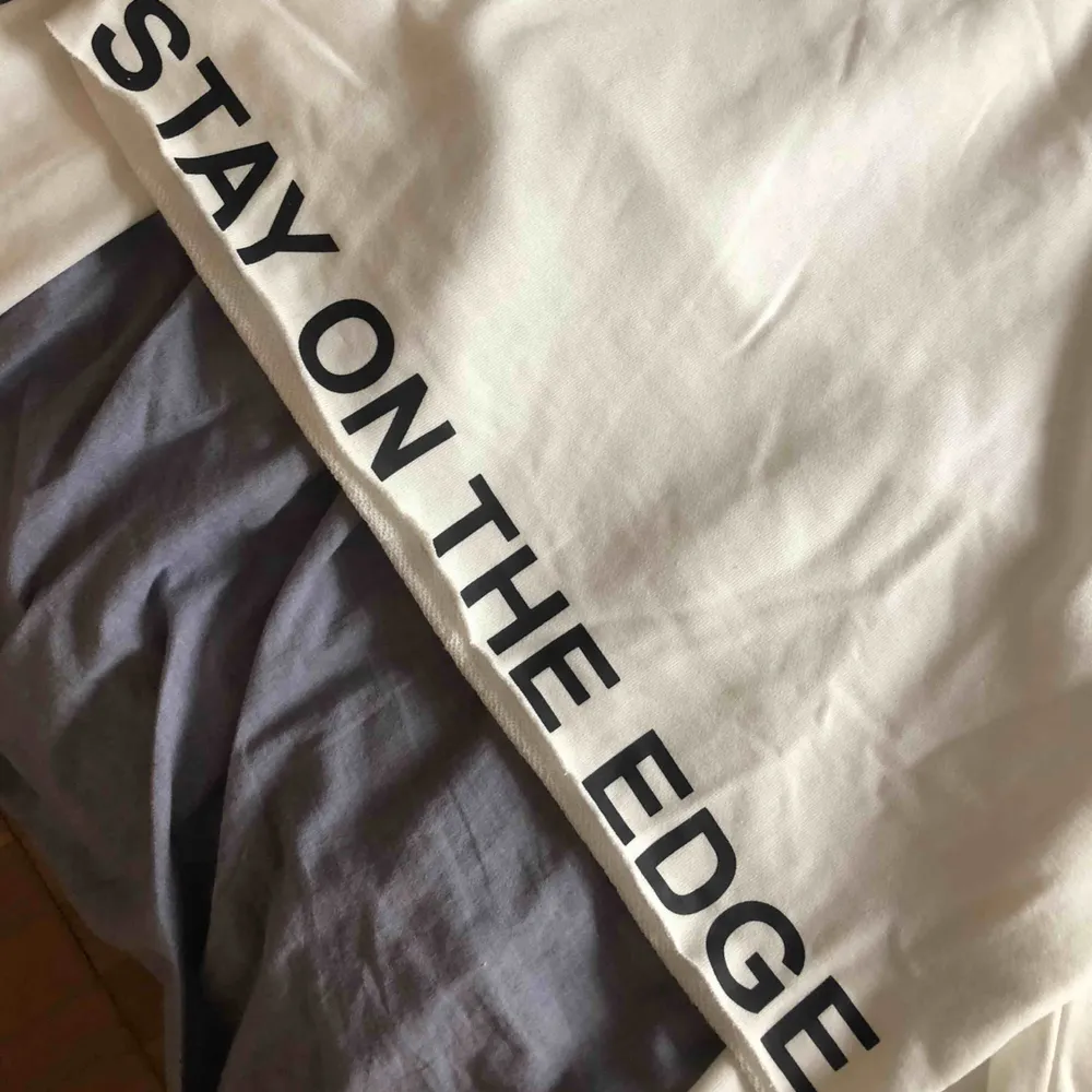 En croppad, långärmad tröja. Vit med svart text - ”stay on the edge” längs framkanten. Använd några enstaka gånger. . Tröjor & Koftor.