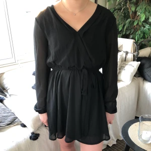 Klänning - Svart omlottklänning med knyte i midjan från Nelly i storlek 40, liten i storlek, skulle säga mer som en 38!😊 150kr plus frakt som köparen står för!