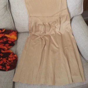 Guldig långklänning - Ytterst användbar och bekväm långklänning med smala axelband. Något syntetiskt, aningens stretchigt och silkigt,  lite tjockare material. Köpt tidigt 00-tal. Frakt tillkommer.