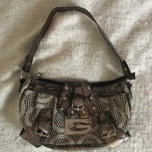 Guess väska - Liten brun väska med silverdetaljer från Guess. Köpt second hand. Tar bud från 125kr, frakt är exkluderat. <3