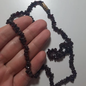 Halsband med mörklila stenar  - Ett oanvänt halsband från Nepal. Svårt att fånga färgen på bild men skulle kalla den mörklila, åt det vinröda hållet. Skriv för fler bilder eller mått. Frakt 11 kr. Se min profil för fler smycken.