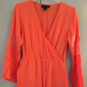  - Jumpsuit. Fickor fram. Dold Dragkedja i sidan. Infälld spets i armar och på längst ned. Endast använd en gång.