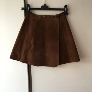  - Äkta vintage mocka-kjol i "skater" modell. Köpt på myrorna. Använd 1 gång. Väldigt hård och stel i materialet. 6 knappar som går att reglera utifrån hur tight man vill ha det i midjan. Köparen står för frakten! Tar helst emot betalning via swish! 