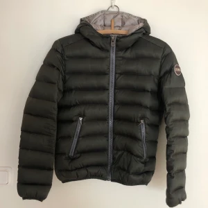 colmar dunjacka storlek xs/ s - Mörkgrön dunjacka från Colmar, storlek 36 (italiensk storlek 42), passar en 34-36. Fint skick förutom en fläck på insidan som kmr från ett klistermärke (syns på sista bilden). 