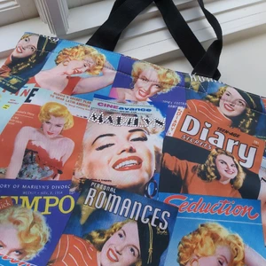 Marilyn Monroe väska - Supersnygg väska men Marilyn Monroe motiv på. Handtagen är 20cm långa och går utmärkt att ha på axeln, i armvecket eller i handen. Inuti är det som ett stort fack. Cool detalj med stenar på framsidan som skriver Marilyn. Botten är 12x28cm. Buda från 80kr