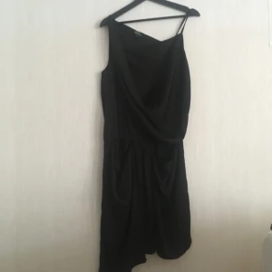  - Svart asymmetrisk klänning med resor i midjan och sidofickor. Knappt använd!  Kan hämtas i Göteborg eller skickas. Köparen står för frakten! 
