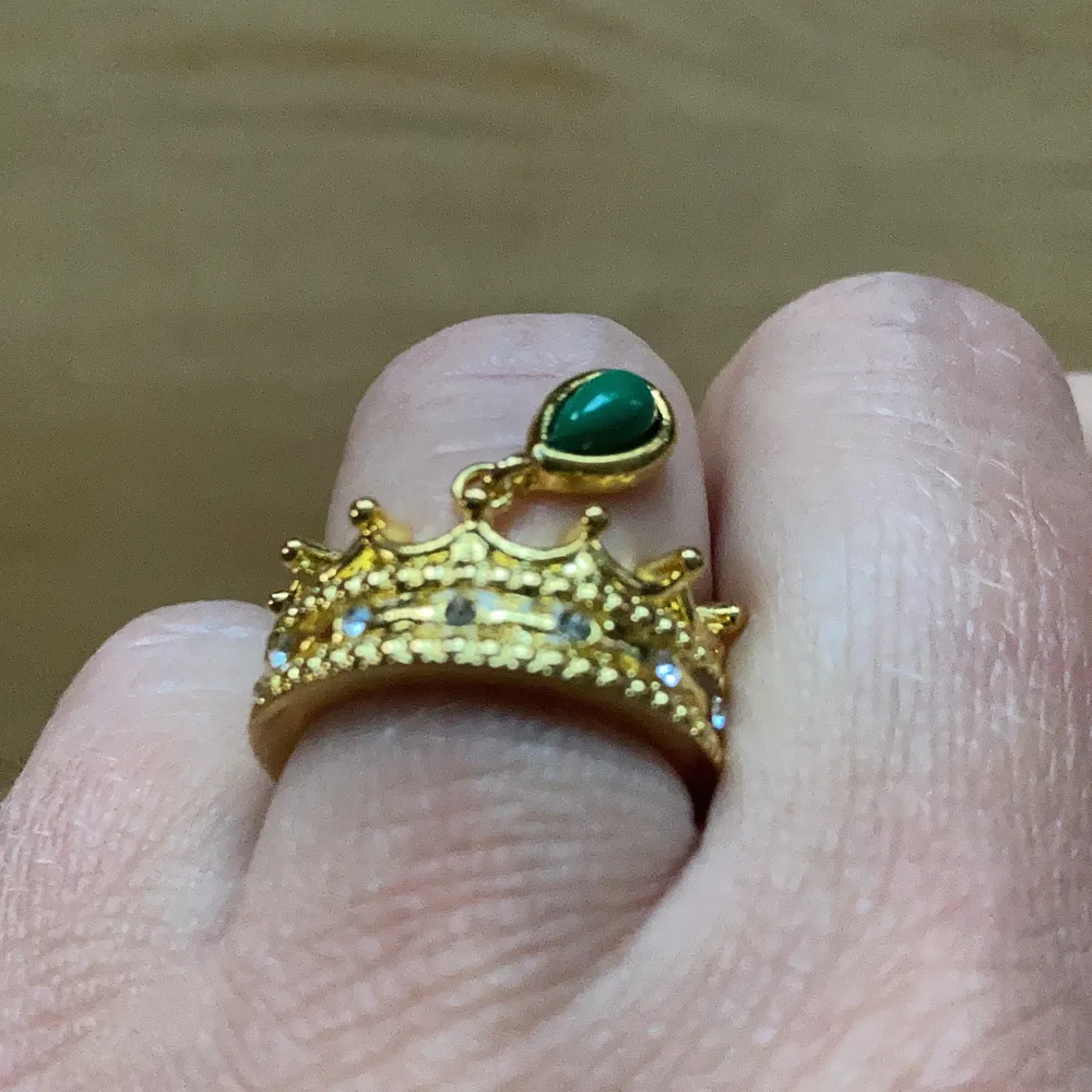 Otroligt söt helt ny ring i guldfärg ca 16,7 mm. Är formad som en krona med vita gnistrande stenar och en grön hängande pärla. . Accessoarer.