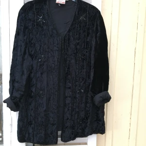 Svart broderad kofta/jacka blommor retro - En supervacker svart jacka/kofta med broderier i form av blommor och paljetter. Fodrad i svart satintyg. Jättefint hantverk! St 38-44 beroende på hur man vill att den ska sitta. I utmärkt skick!