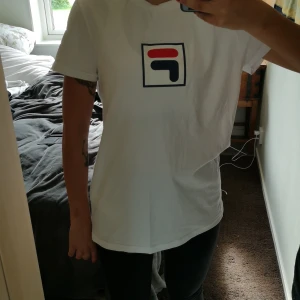 T-shirt - T-shirt ifrån Fila. Vit med ett märke på bröstet. Lite längre än vanlig modell. Unisexmodell. 