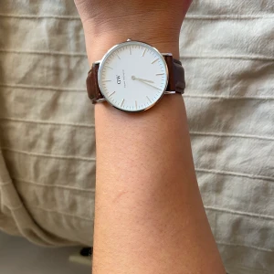 Silvrig Daniel Wellington klocka  - Jätte fin klocka från Daniel Wellington köpt 2017. Använd fåtal gånger & är nästan som ny. Batteriet är tyvär slut, men går att köpa ny. 