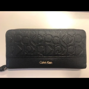 Calvin Klein clutch/plånbok - Super fin svart guldig clutch plånbok från Calvin Klein. I fint skick med någon liten repa på guld dragkedjan. Köpt för 900kr i butik
