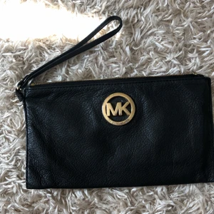 Michael Kors clutch - Svart clutch med guldmärke från Michael Kors. Inköpt i USA. Nypris ca 1000kr. MK-märket har tydliga repor och dragskon är borta därav det otroligt billiga priset (se bild 3). Köparen står för frakt!