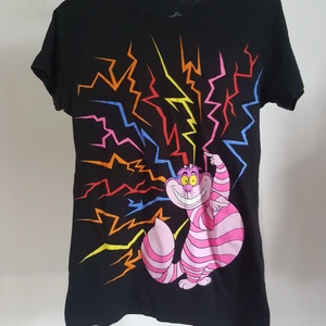 T-Shirt Filurkatten - T-shirt med Filurkatten från Alice i underlandet. Märket är Disney Couture och är köpt i Kanada för några år sen. Använd några gånger. Notera att det är märke på filurkatten samt ett hål i armhålan som säkert går att sy. Storlek M/M. Thight/"kvinnlig" passform. Frakt ingår.