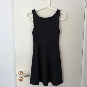  - Svart klänning i elastiskt ”bikini-tyg” från H&M, med djup V-ringning i ryggen. Supersnygg modell, med åtsittande på överkropp ner till midjan och därefter vippig nedtill. Använd en gång.