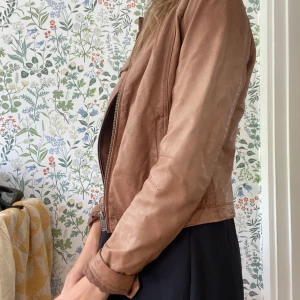 skinnjacka - En skinnjacka i färgen cognac från jofama. Naturligt sliten i skinnet vilket ger en snygg look. Aningen figursydd. Bra skick men använd.