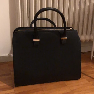 Fakeläder handväska - Det är en svart fakeläder handväska med ett axelband du kan sätta på eller ta av. Den har en trasig knapp men det märks inte så tydligt. Använd 1 gång. 