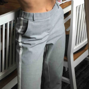  - Grå ”kostymbyxor” i mjukt material med vit revär på sidan. I storlek XS men kan passa även en S om man vill ha dem tightare. Använda några gånger men i fint skick, så gott som nytt!