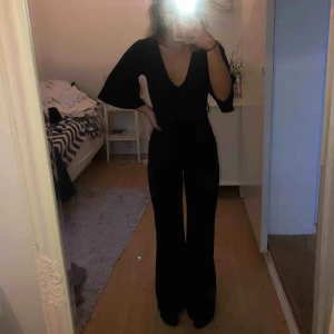  - Svart jumpsuit från Missguided med vida ärmar och ben. Djup v-rigning och band att knyta i midjan. Benen är uppsydda så att den ska passa någon som är 160-165 cm. Aldrig använd. Köparen betalar frakten.