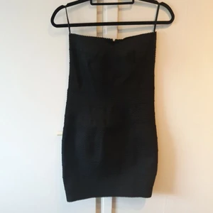 Svart klänning  - Helt oanvänd liten svart klänning med detaljerat tjockare tyg som formar klänningen. Även detaljerat vid bysten. Dragkedja i ryggen och finns ett extra spänne vid toppen av dragkedjan. Det är en tubklänning (?)