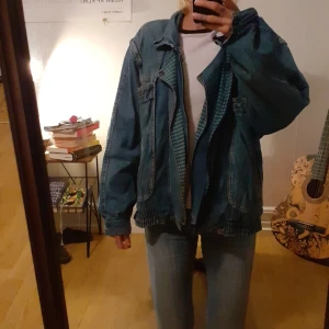 Jeansjacka med avtagbara ärmar - Blå jeansjacka med dragkedja samt dragkedje-avtagbara ärmar så att det istället blir en väst. Rutigt mönstrad insida.  2 Bröstfickor, 2 sidofickor och 2 innerfickor.