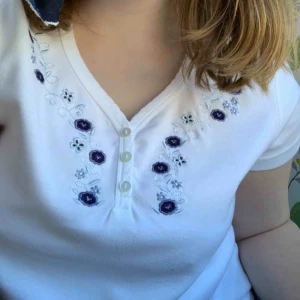  - Fin t-shirt som liknar de trendiga brandy Melville topparna. Knappar och broderade blommor. Superfin till sommaren. Perfekt skick. Står markerad som L men är mer som S eller M. Fri frakt!