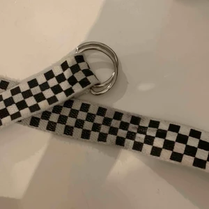  - Checkered bälte som är ca 1 meter långt. Den var längre innan men har klippt av en del av den, dock märks det knappt att det är avklippt. Bältet har blivit lite grått just där jag spänt åt det 